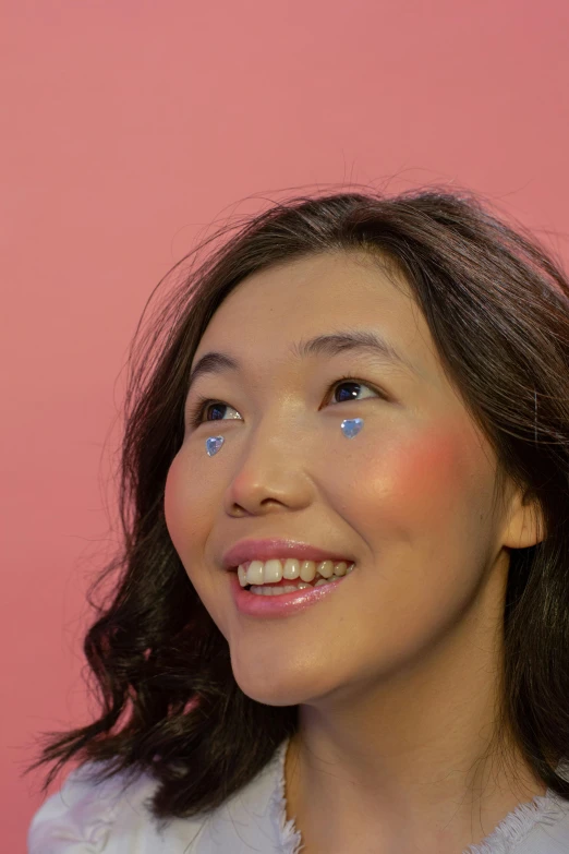 a woman standing in front of a pink wall, an album cover, inspired by Russell Dongjun Lu, trending on pexels, hyperrealism, iridescent eyes, mole on cheek, ethnicity : japanese, high angle closeup portrait