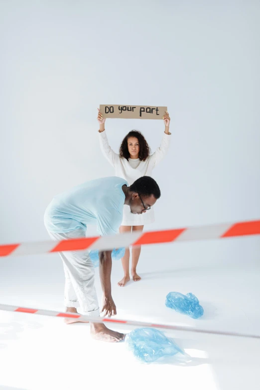 a man standing next to a woman holding a sign, an album cover, by Matija Jama, pexels contest winner, antipodeans, performance art, spilled milk, virgil abloh, crime scene