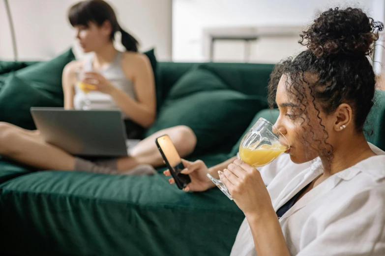 a woman sitting on a couch drinking a glass of orange juice, trending on pexels, happening, two models in the frame, mobile game, someone sits in bed, teenager hangout spot