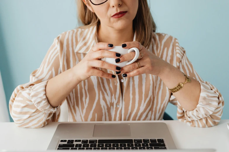a woman sitting in front of a laptop holding a cup, by Julia Pishtar, trending on pexels, square rimmed glasses, delicate patterned, awkward, low quality photo