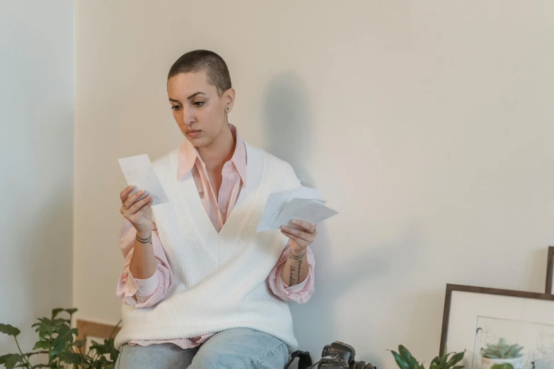 a woman sitting on a bed reading a book, a photo, by Emma Andijewska, pexels contest winner, hyperrealism, shaved head, with some hand written letters, tarot cards characters, holly herndon origami statue