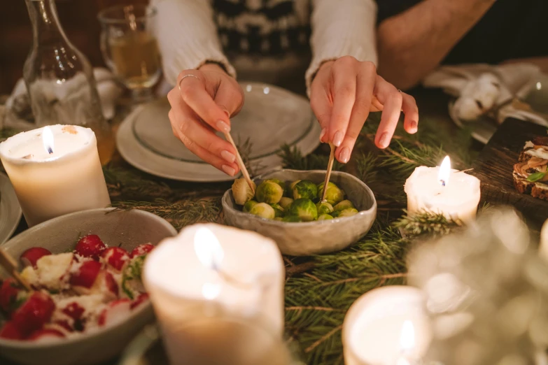 a person sitting at a table with a bowl of food, by Daniel Lieske, pexels contest winner, arts and crafts movement, christmas night, white candles, square, greens)