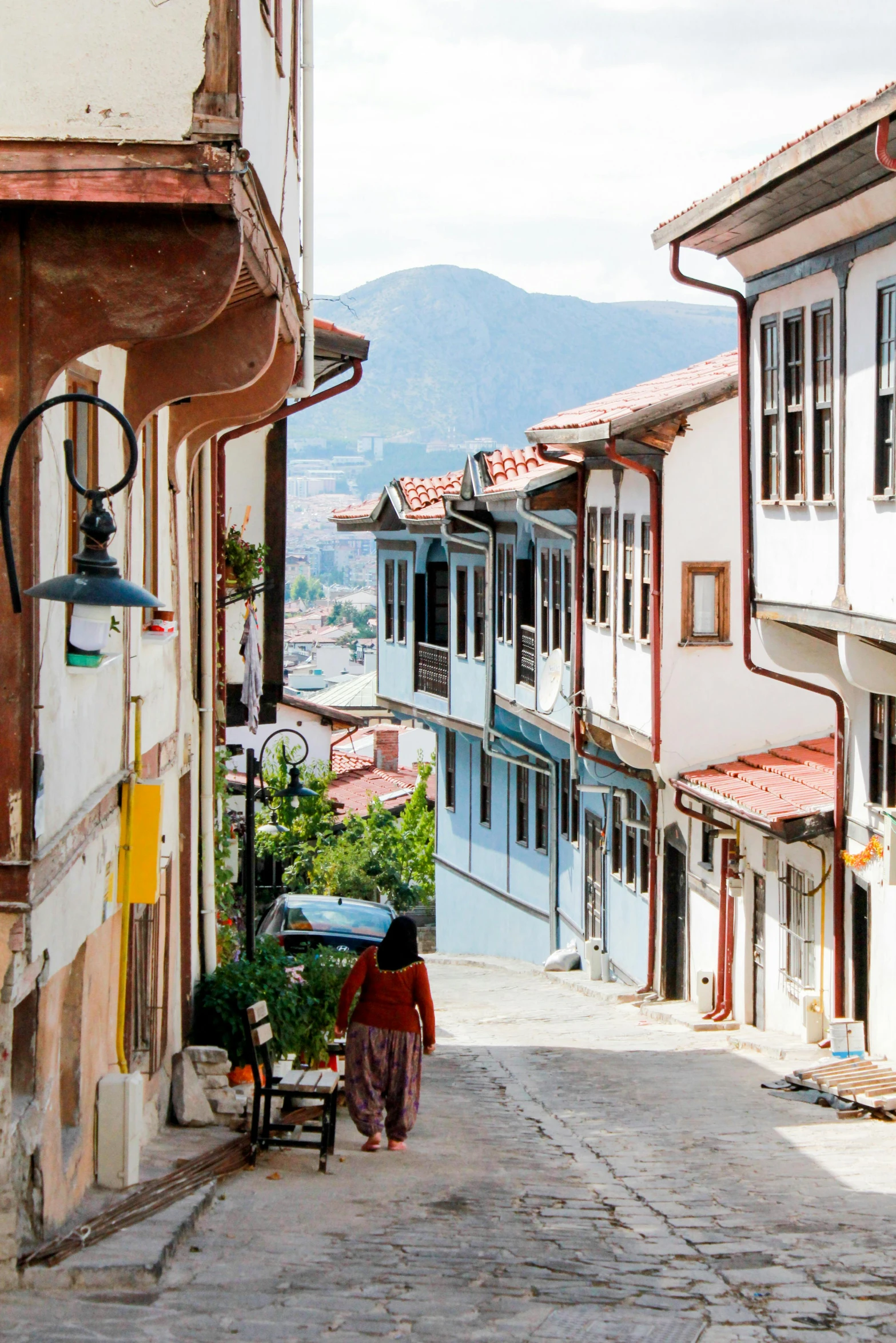 a woman walking down a narrow cobblestone street, inspired by Niyazi Selimoglu, trending on unsplash, art nouveau, bhutan, houses on stilts, turkey, square