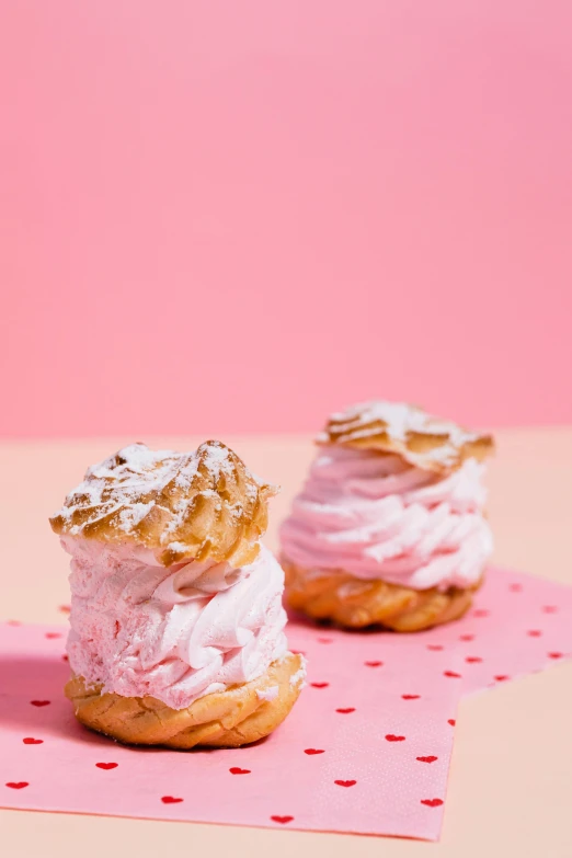 a couple of pastries sitting on top of a pink napkin, whipped cream on top, pink background, f/2.5, sea of parfait