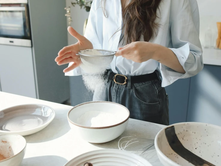 a woman standing in a kitchen preparing food, inspired by Yukimasa Ida, trending on pexels, white clay, glass tableware, background image, flour dust