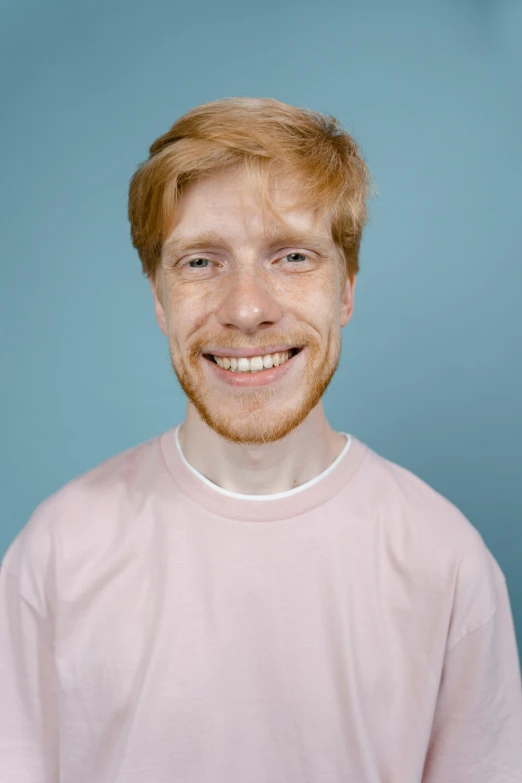 a man in a pink shirt posing for a picture, by Jacob Toorenvliet, ginger hair, wearing a light blue shirt, very very very pale white skin, happily smiling at the camera