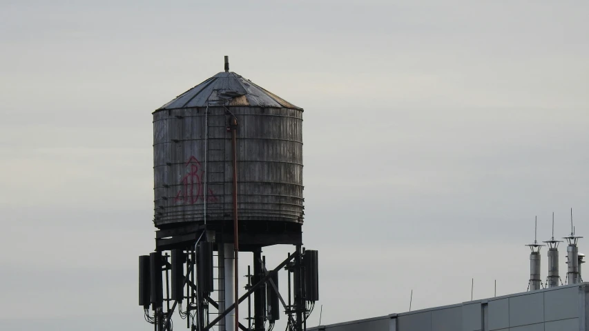 a water tower on top of a building, a photo, flickr, leaking, vessels, gray, metal with graffiti on the side