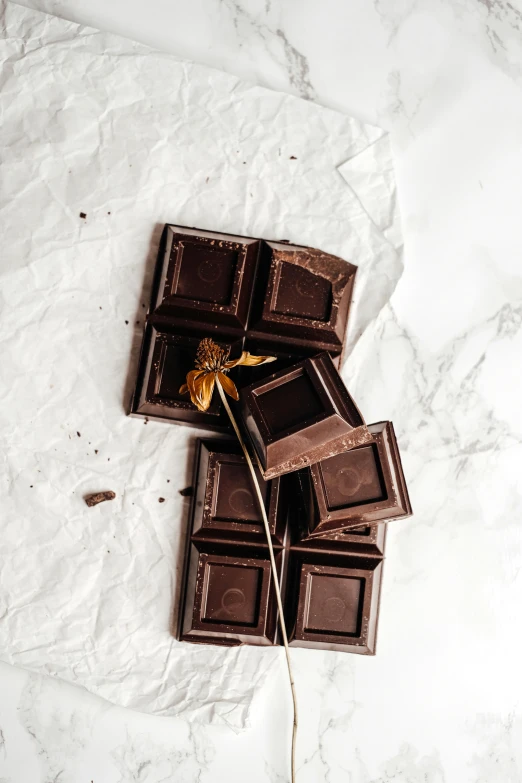 a piece of chocolate sitting on top of a piece of paper, a still life, trending on pexels, baroque, black squares on 4 corners, gold flaked flowers, edible, 6 pack