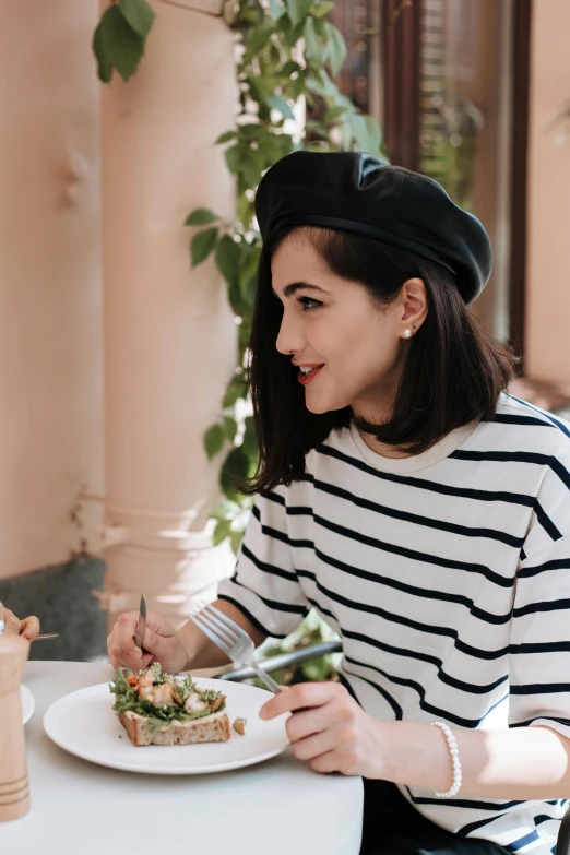 a woman sitting at a table with a plate of food, wearing a french beret, millennial vibes, profile image, striped