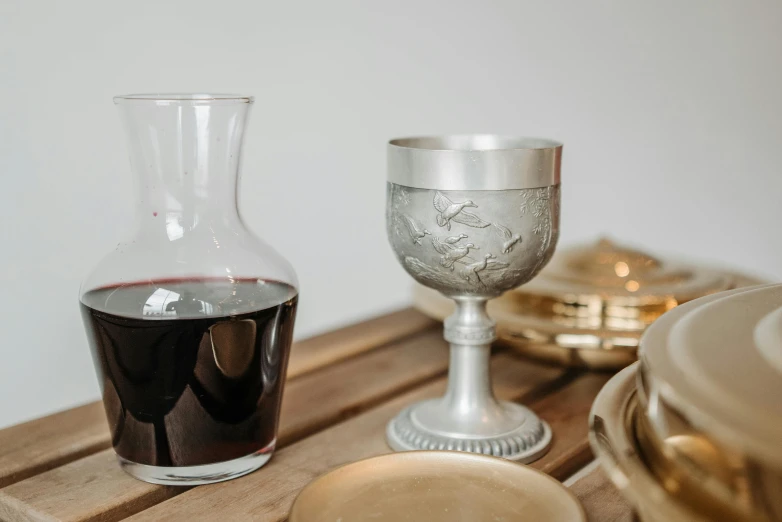 a glass of wine sitting on top of a wooden table, inspired by William Home Lizars, arts and crafts movement, grey and silver, priest, cast, silver glasses