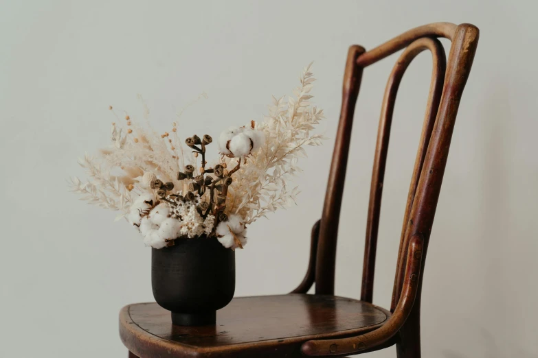 a black vase sitting on top of a wooden chair, by Carey Morris, trending on unsplash, dried flowers, cream and white color scheme, seated on a throne, single chair