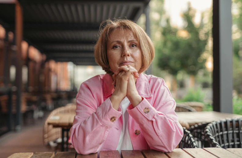 a woman sitting at a table in a restaurant, a portrait, pexels contest winner, realism, pink, portrait 6 0 - year - old woman, calm weather, 15081959 21121991 01012000 4k