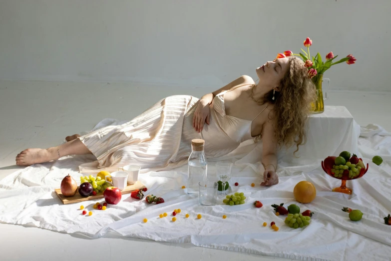 a beautiful woman laying on top of a white blanket, a still life, inspired by Konstantin Somov, unsplash, renaissance, bedazzled fruit costumes, !!posing_as_last_supper, on a white table, organic dress