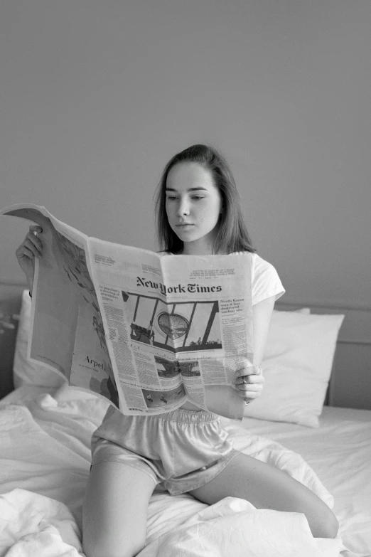 a woman sitting on a bed reading a newspaper, a black and white photo, by Felix-Kelly, pexels contest winner, 1 6 years old, 3 d, pout, gif