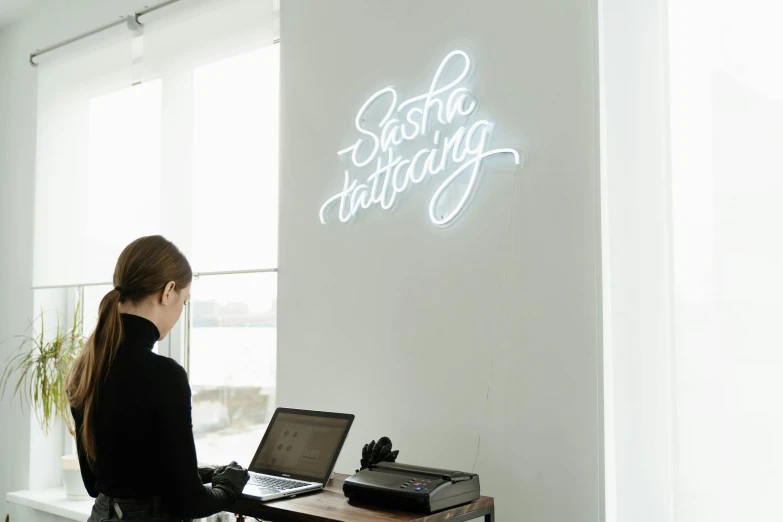 a woman sitting at a desk with a laptop, a silk screen, by Sebastian Spreng, trending on unsplash, interactive art, white neon lighting, waiting room, on a white table, calligraphy