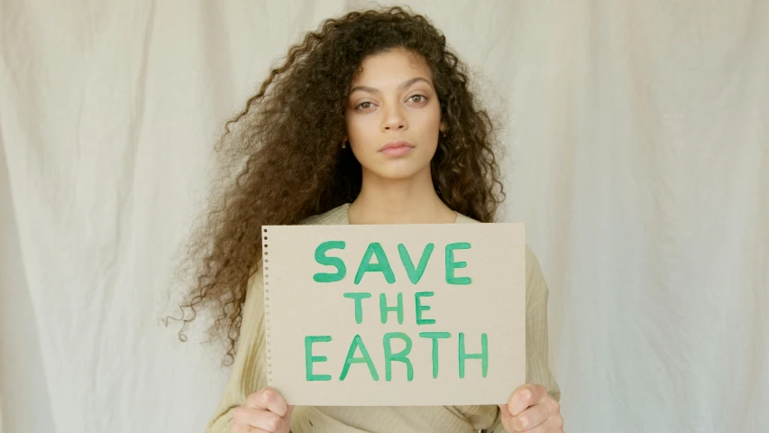 a woman holding a sign that says save the earth, an album cover, trending on pexels, renaissance, skincare, lorde, beige, sustainable