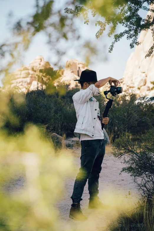 a man standing on a dirt road holding a camera, standing next to desert oasis, in an action pose, unsplash transparent, amongst foliage