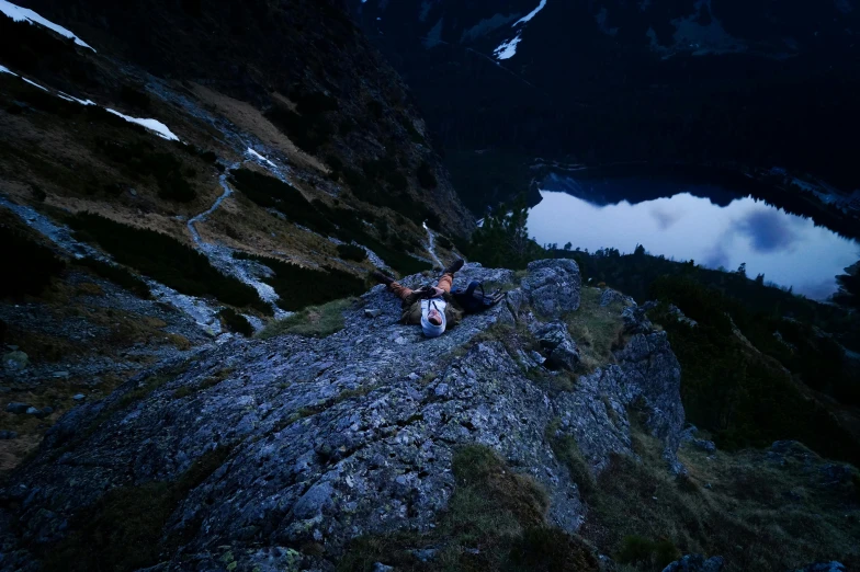 a man sitting on top of a mountain next to a lake, by Jessie Algie, pexels contest winner, sprawled out, late night, avatar image, aerial footage