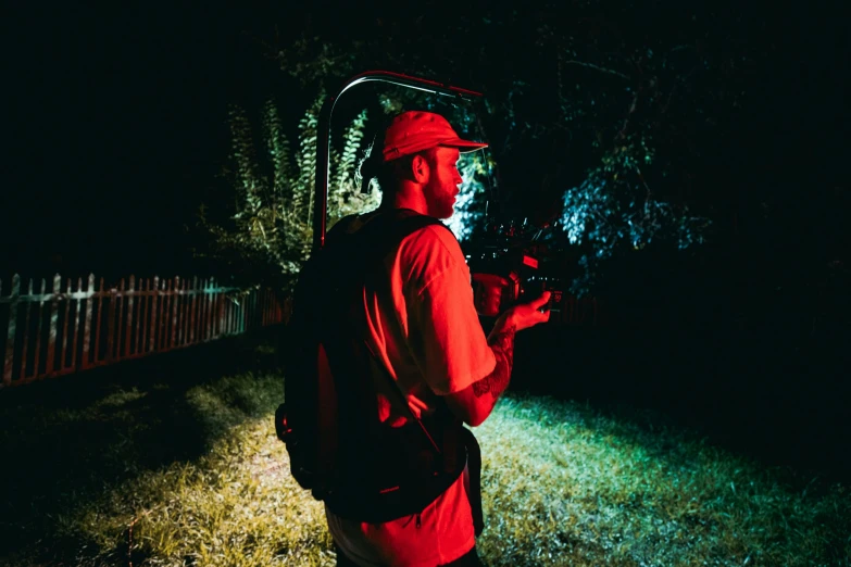 a man standing in the dark holding a baseball bat, red camera, a man wearing a backpack, at night with lights, bladee from drain gang