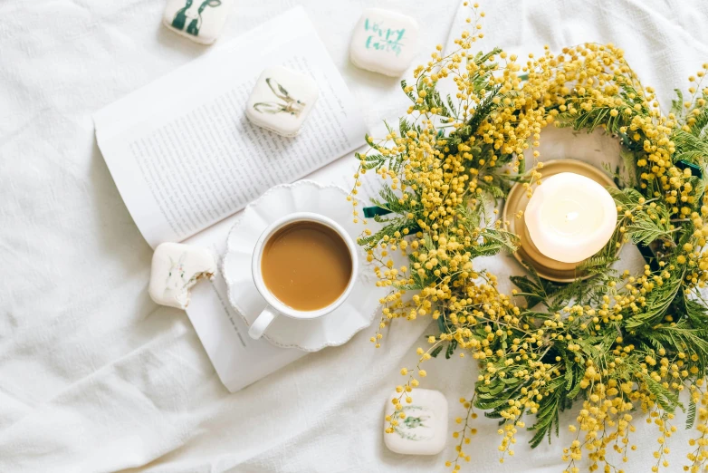 a wreath sitting on top of a bed next to a cup of coffee, by Lucia Peka, pexels contest winner, romanticism, yellow and greens, tea drinking and paper lanterns, manuka, on a white table