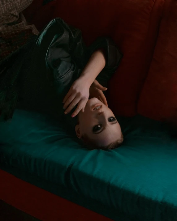 a woman laying on top of a red couch, inspired by Elsa Bleda, trending on pexels, visual art, androgynous male, dark teal couch, joey king, looking up at the camera