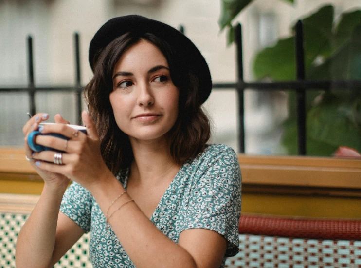 a woman sitting at a table with a cell phone in her hand, a portrait, by Julia Pishtar, trending on pexels, it's wearing a cute little hat, french girl, middle length hair, charli bowater