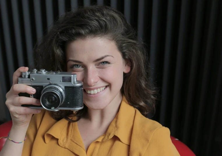 a woman holding a camera in front of her face, smirking at the camera, taken on a ww 2 camera, portrait photo of a backdrop, commercial photograph