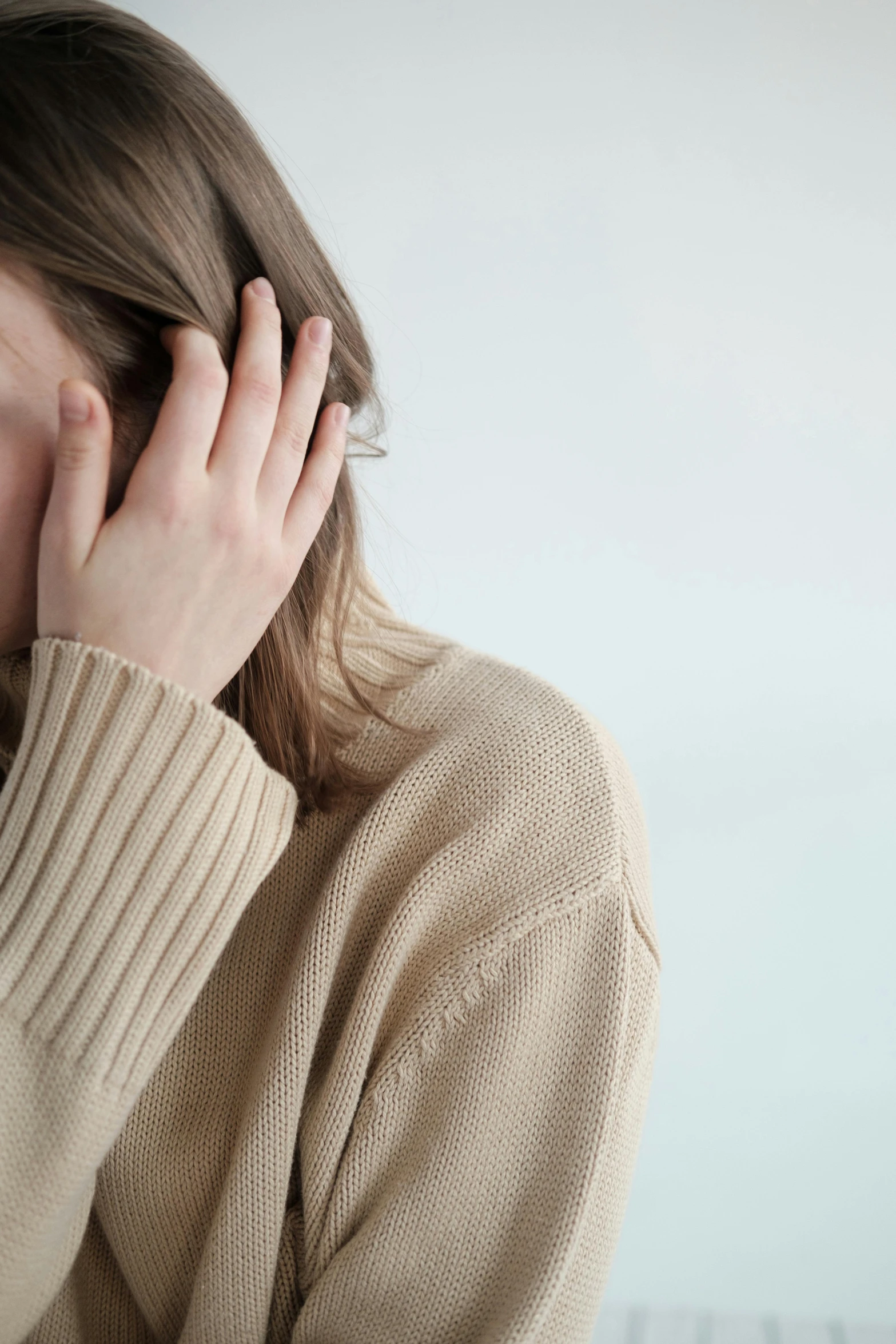 a woman covering her face with her hands, he is wearing a brown sweater, light borwn hair, she is distressed, wearing a white sweater