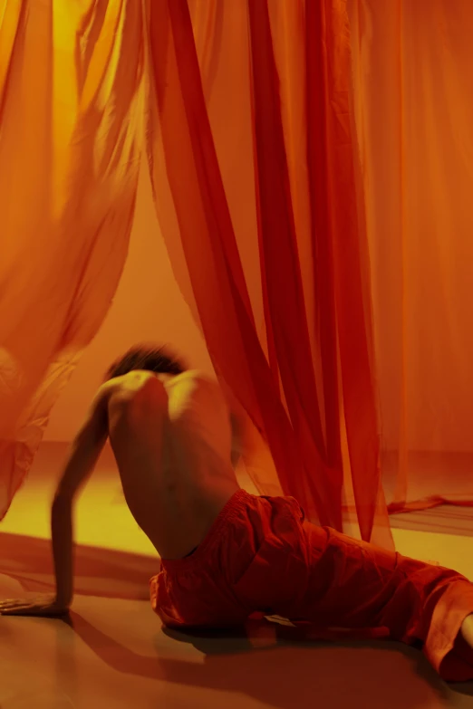 a man laying on the floor in front of a curtain, by Nathalie Rattner, arabesque, orange and red lighting, silks, showstudio, yellow and red