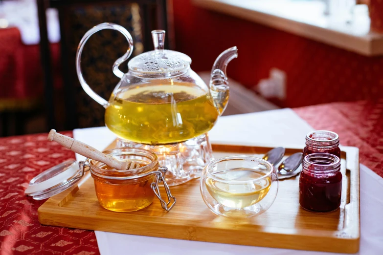 a tea pot sitting on top of a wooden tray, by Julia Pishtar, pexels, jar of honey, on a sumptuous tablecloth, jelly, green tea