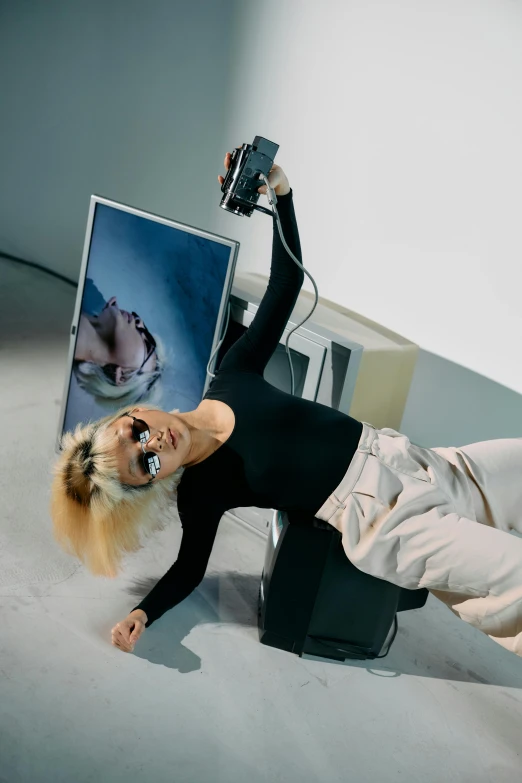 a woman laying on top of a bed holding a camera, inspired by Gao Cen, video art, doing a sassy pose, white hair floating in air, with square glasses, in a museum