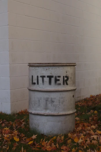 a metal barrel sitting in the grass next to a building, by Ben Zoeller, trash can, in white lettering, during autumn, gray