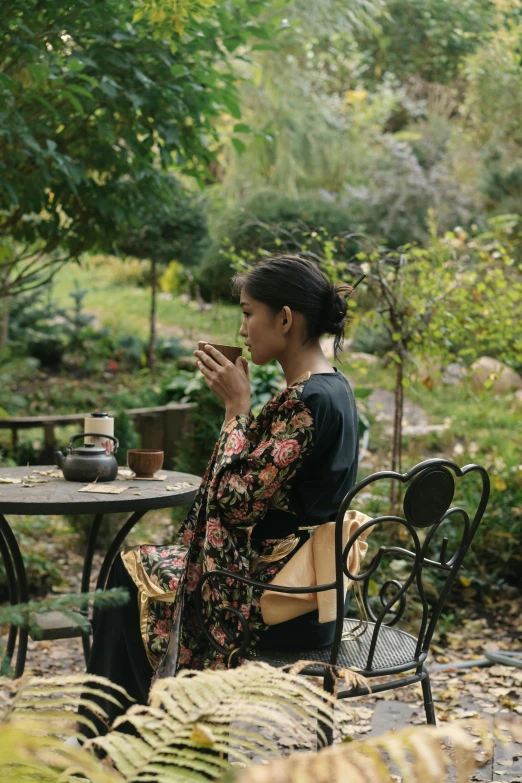 a woman sitting at a table with a cup of coffee, inspired by Cui Bai, unsplash, cloisonnism, in garden, wearing black silk robes, medium format, 8 k )