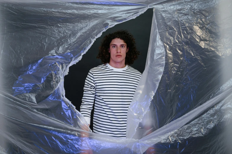 a man standing in a room covered in plastic, an album cover, inspired by Christo, pexels contest winner, curly haired, containment pod, white holographic plastic, dark backdrop