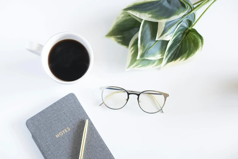 a cup of coffee and a notebook on a table, by Carey Morris, pexels contest winner, minimalism, square glasses, plants in glasses, gold glasses, on a white background