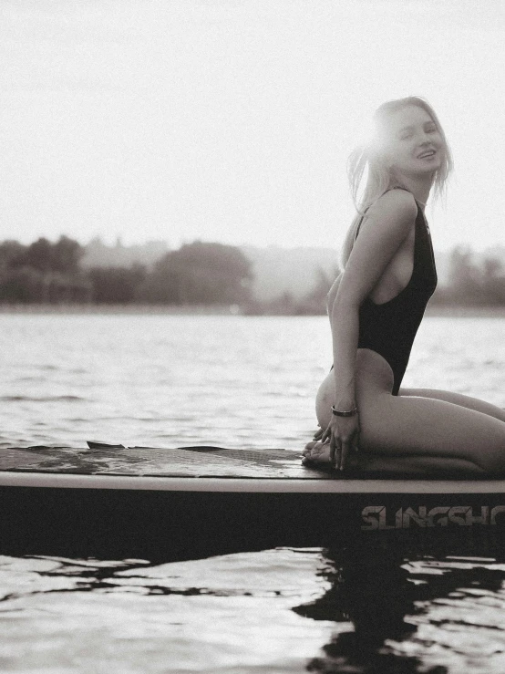 a woman sitting on a surfboard in the water, a black and white photo, unsplash, renaissance, cute girl wearing tank suit, on a boat on a lake, sunfaded, olga buzova