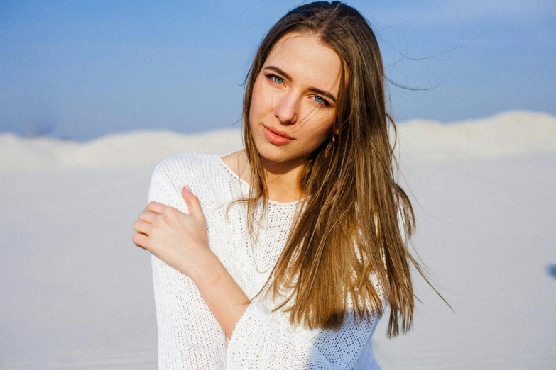 a beautiful young woman standing on top of a sandy beach, a portrait, by Julia Pishtar, pexels contest winner, tachisme, wearing a white sweater, light brown hair blue eyes, modelling, russian girlfriend