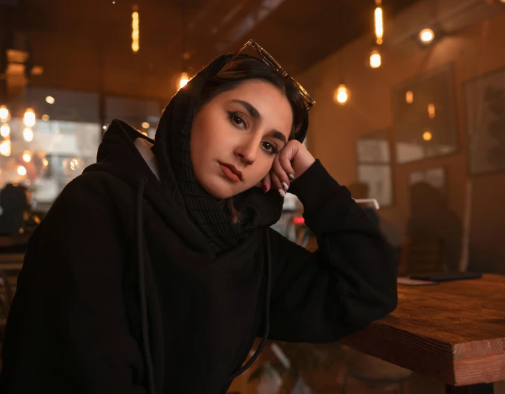 a woman sitting at a table talking on a cell phone, a portrait, trending on pexels, hyperrealism, in a black hoodie, beautiful iranian woman, dramatic serious pose, sitting in a cafe