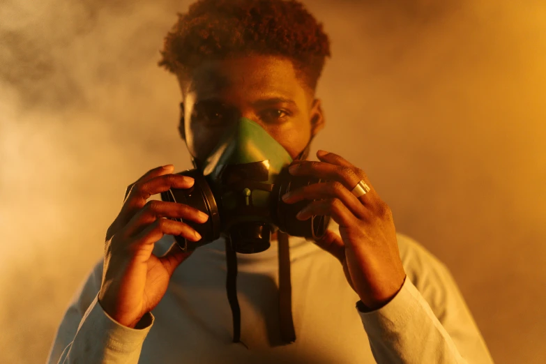 a man holding a gas mask in front of his face, afrofuturism, smoke filled room, photoshoot for skincare brand, profile image, holding green fire