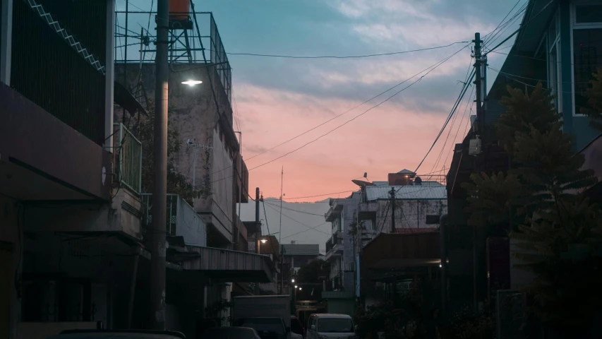 a street filled with lots of cars next to tall buildings, a picture, inspired by Elsa Bleda, pexels contest winner, pink sunset hue, wires hanging above street, standing in a township street, downtown mexico