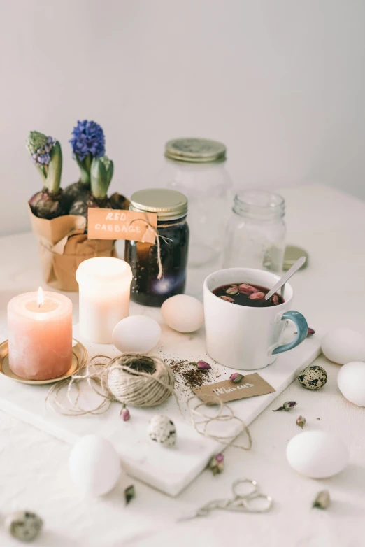 a bunch of candles sitting on top of a table, with a white mug, botanicals, ingredients on the table, springtime morning