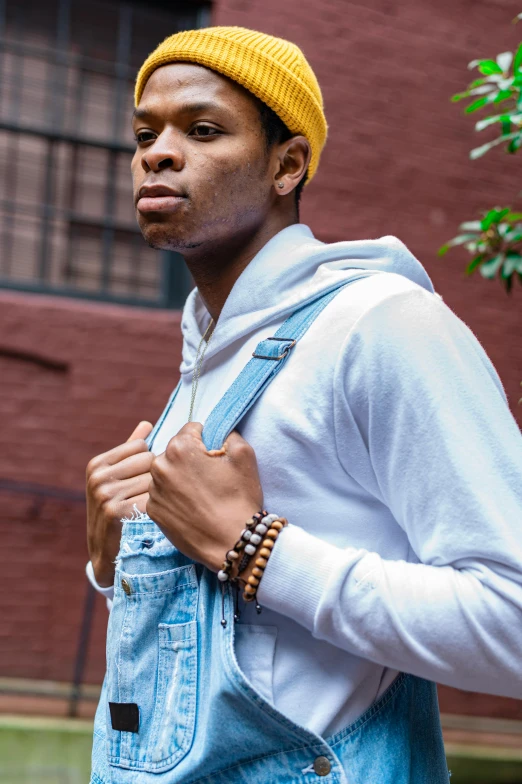 a man wearing a yellow hat and blue overalls, trending on pexels, in style of tyler mitchell, white sleeves, in new york city, wooden jewerly