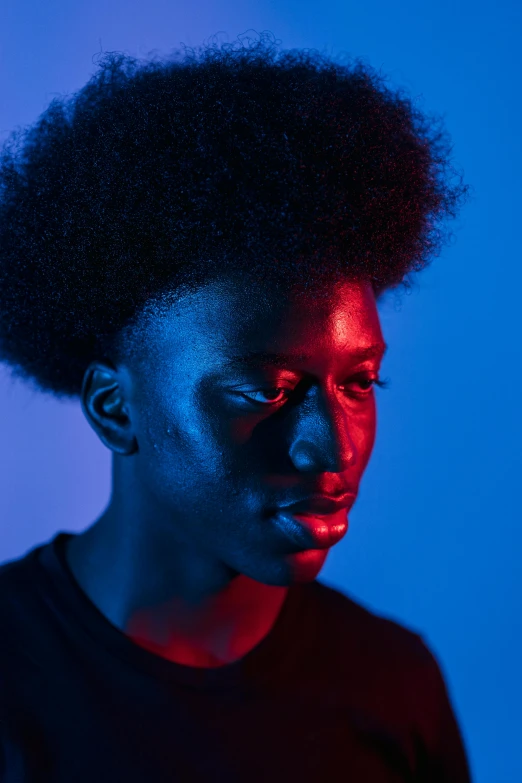 a woman with an afro standing in front of a blue background, by Cosmo Alexander, pexels contest winner, dramatic lighting man, red and blue black light, black teenage boy, pensive expression