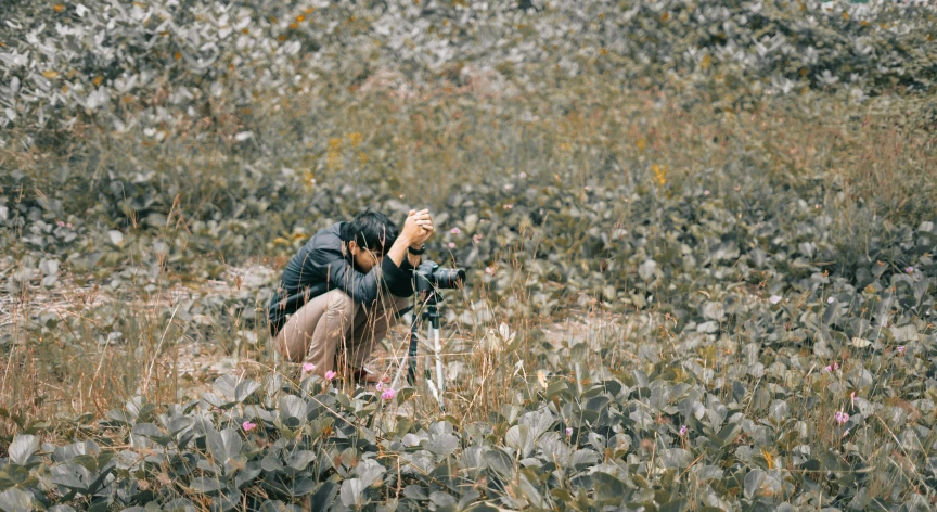 a man kneeling in a field with a camera, by Elsa Bleda, visual art, zezhou chen, flowers around, medium format, autumn