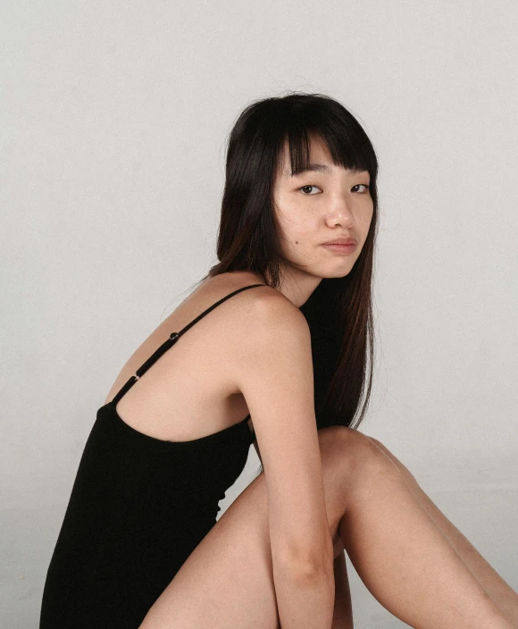 a woman sitting on the floor with her legs crossed, by helen huang, trending on unsplash, realism, she is wearing a black tank top, young cute wan asian face, wearing a black bodysuit, nonbinary model