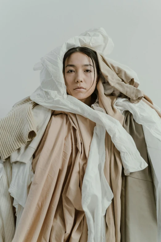 a woman standing in front of a pile of clothes, inspired by Kim Tschang Yeul, unsplash contest winner, gutai group, wearing hay coat, white sleeves, fully covered in drapes, natural muted tones