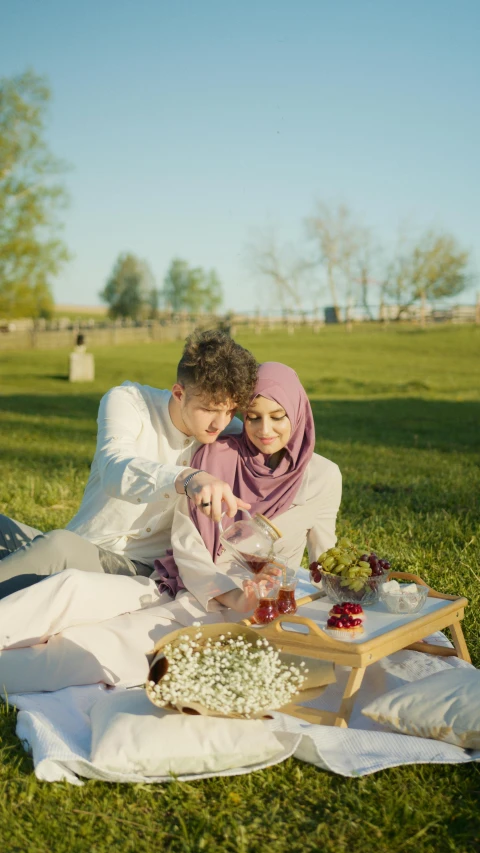 a man and a woman sitting on a blanket in the grass, a colorized photo, by Ismail Acar, pexels, hurufiyya, eating outside, love theme, square, islamic