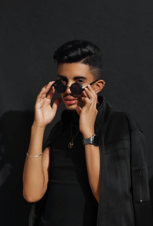 a man standing in front of a black wall talking on a cell phone, an album cover, inspired by Hedi Xandt, trending on pexels, portrait androgynous girl, middle eastern, aviators, black jewerly