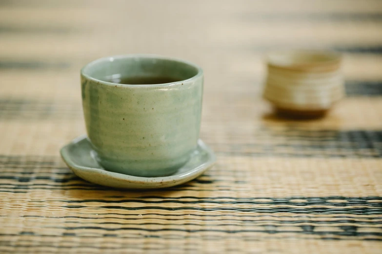 a close up of a cup and saucer on a table, inspired by Tōshi Yoshida, trending on unsplash, mingei, sage green, made of bamboo, fine texture detail, medium format