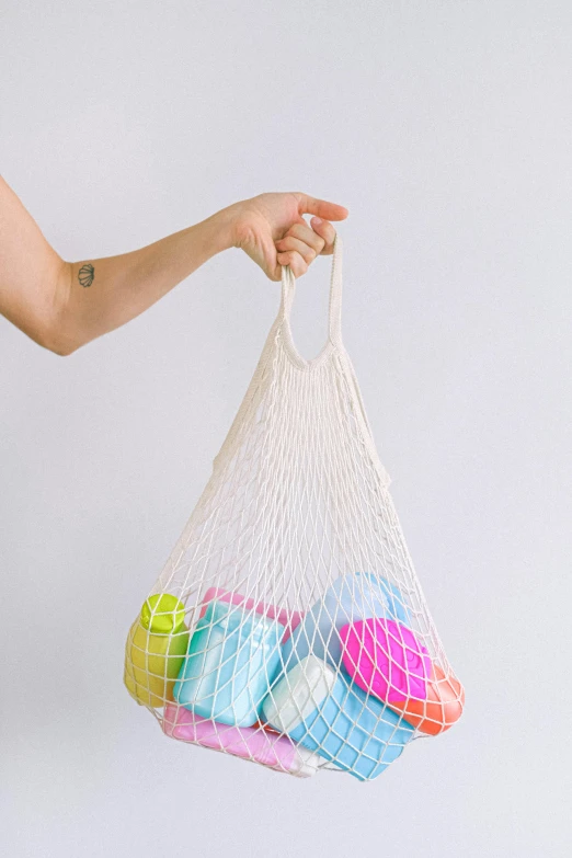 a woman holding a net bag filled with balls, by Jessie Algie, unsplash, plasticien, clean design, promo image, strings, various colors